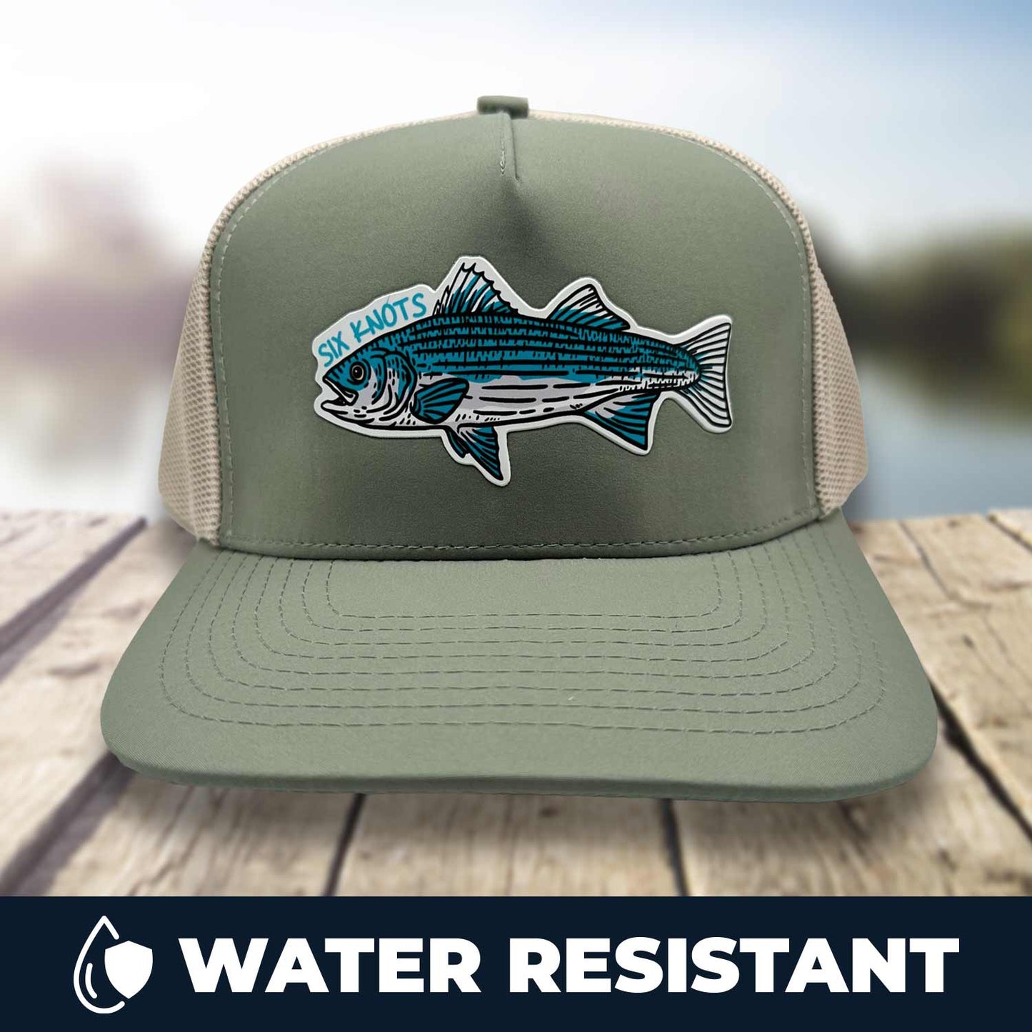 Six Knots Trophy Season Snapback Hat resting on a dock with a blurred marina backdrop — water-resistant performance fishing hat in green and tan, featuring a bold front patch with an embroidered striped bass and Six Knots lettering. Built for durability and breathability, ideal for saltwater fishing, offshore boating, and rugged all-weather coastal lifestyle wear.