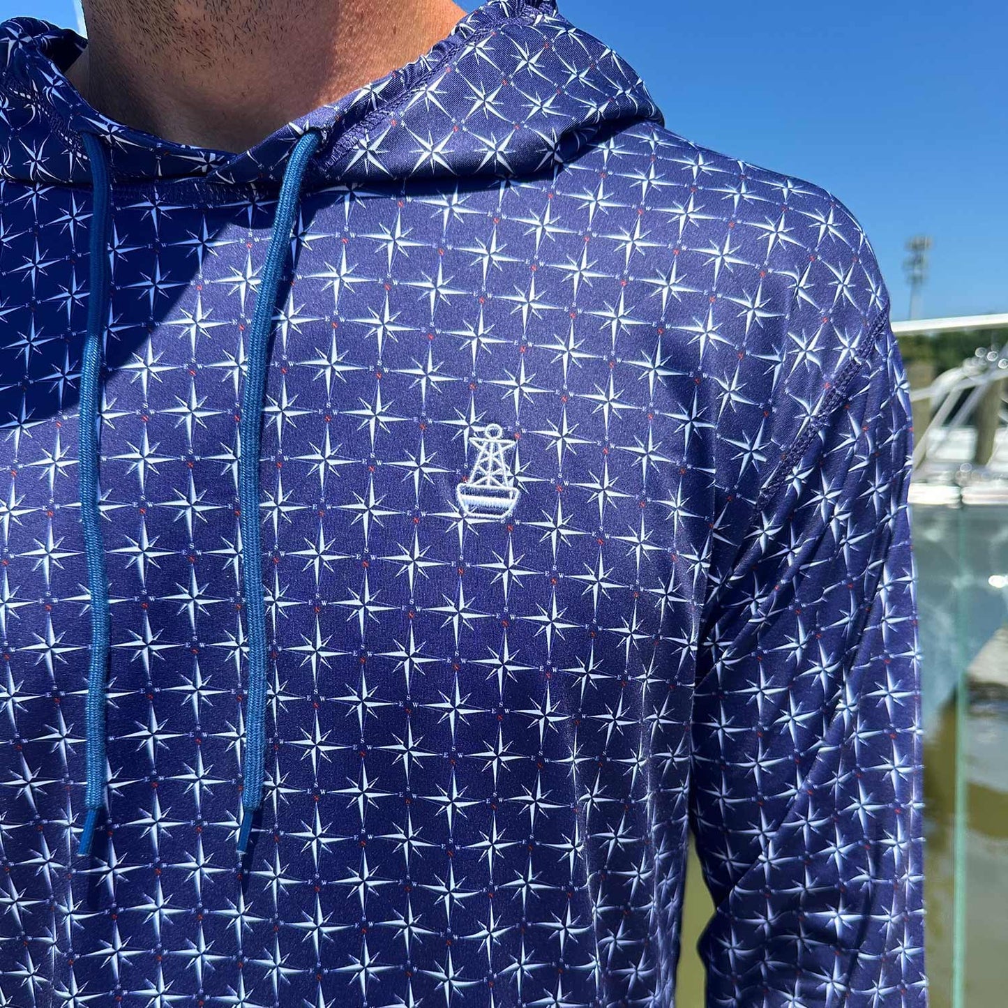 Close-up of the Six Knots True North Men's Performance Hoodie in navy, highlighting the detailed compass pattern and signature Six Knots buoy logo. This lightweight, moisture-wicking hoodie features UPF sun protection and quick-dry performance—ideal for boating, saltwater fishing, and warm-weather coastal adventures.
