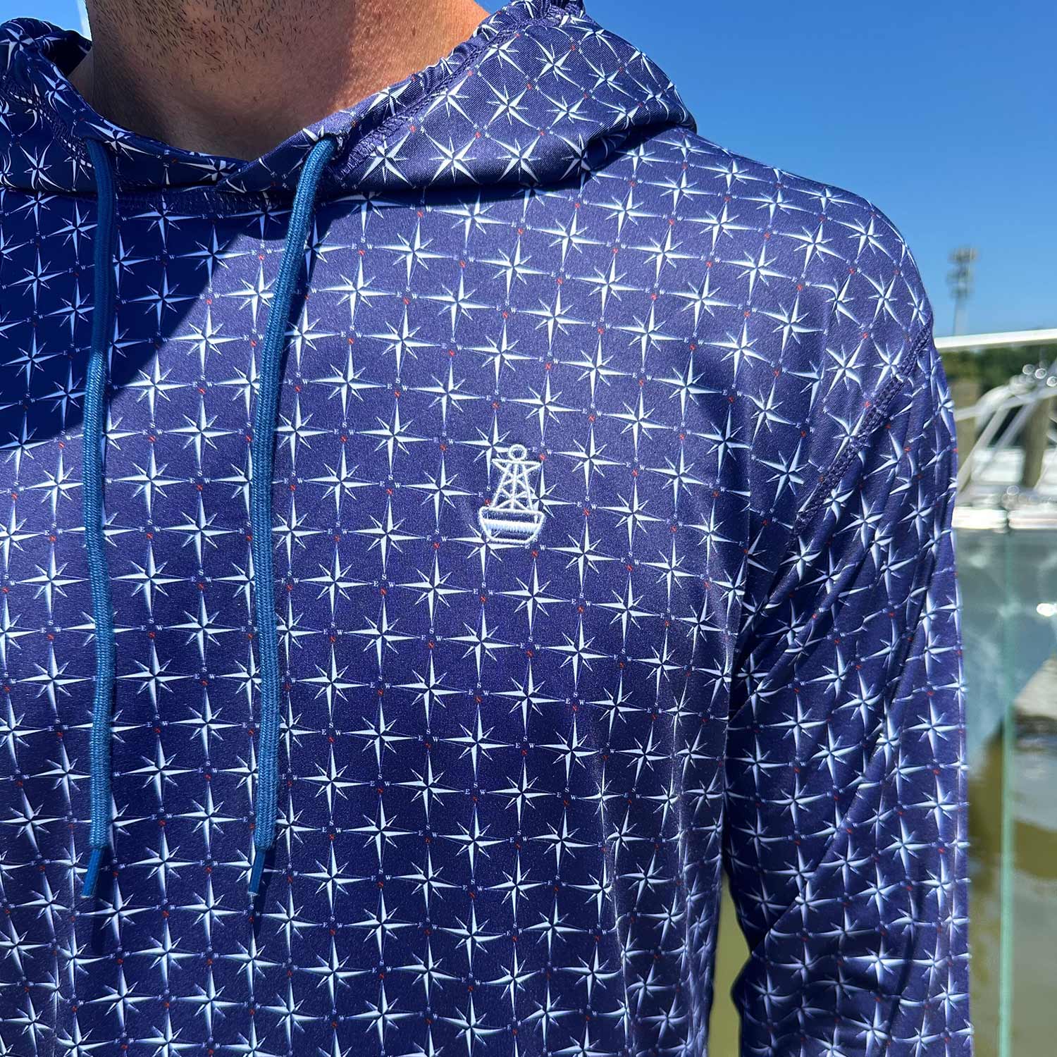 Close-up of the Six Knots True North Men's Performance Hoodie in navy, highlighting the detailed compass pattern and signature Six Knots buoy logo. This lightweight, moisture-wicking hoodie features UPF sun protection and quick-dry performance—ideal for boating, saltwater fishing, and warm-weather coastal adventures.