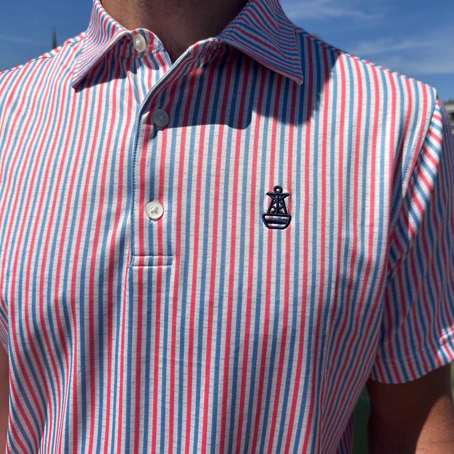 Close-up of the front of the Six Knots All American Performance Polo Shirt featuring the signature buoy logo and patriotic red, white, and blue seersucker stripes — lightweight, moisture-wicking men's polo ideal for fishing, boating, golf, and summer wear