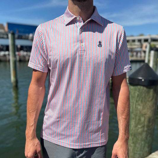 Man wearing the Six Knots All American Performance Polo Shirt on a marina dock, showcasing patriotic red, white, and blue seersucker stripes — breathable, moisture-wicking men's polo perfect for fishing, boating, golf, and summer activities