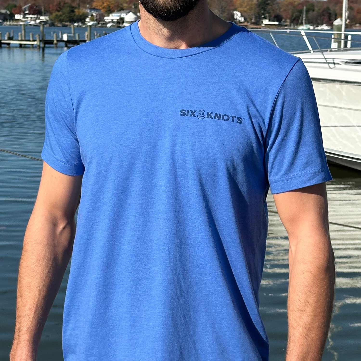 Man at a Maryland marina wearing the blue Six Knots American Buoy Classic T-Shirt. This lightweight, ultra-soft unisex tee is made from a breathable cotton-polyester blend and features a subtle Six Knots wordmark on the chest. Perfect for everyday wear, weekend relaxation, coastal getaways, casual outings, and easygoing waterfront style.
