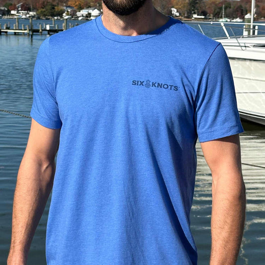 Man at a Maryland marina wearing the blue Six Knots American Buoy Classic T-Shirt. This lightweight, ultra-soft unisex tee is made from a breathable cotton-polyester blend and features a subtle Six Knots wordmark on the chest. Perfect for everyday wear, weekend relaxation, coastal getaways, casual outings, and easygoing waterfront style.