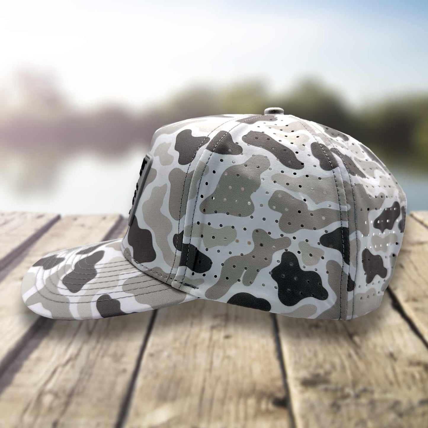 Side view of the Six Knots Coastal Camo Snapback Hat on a dock with a blurred marina backdrop, highlighting the breathable mesh back — water-resistant camo performance hat featuring a gray camouflage pattern; perfect for fishing, boating, and versatile coastal lifestyle wear.