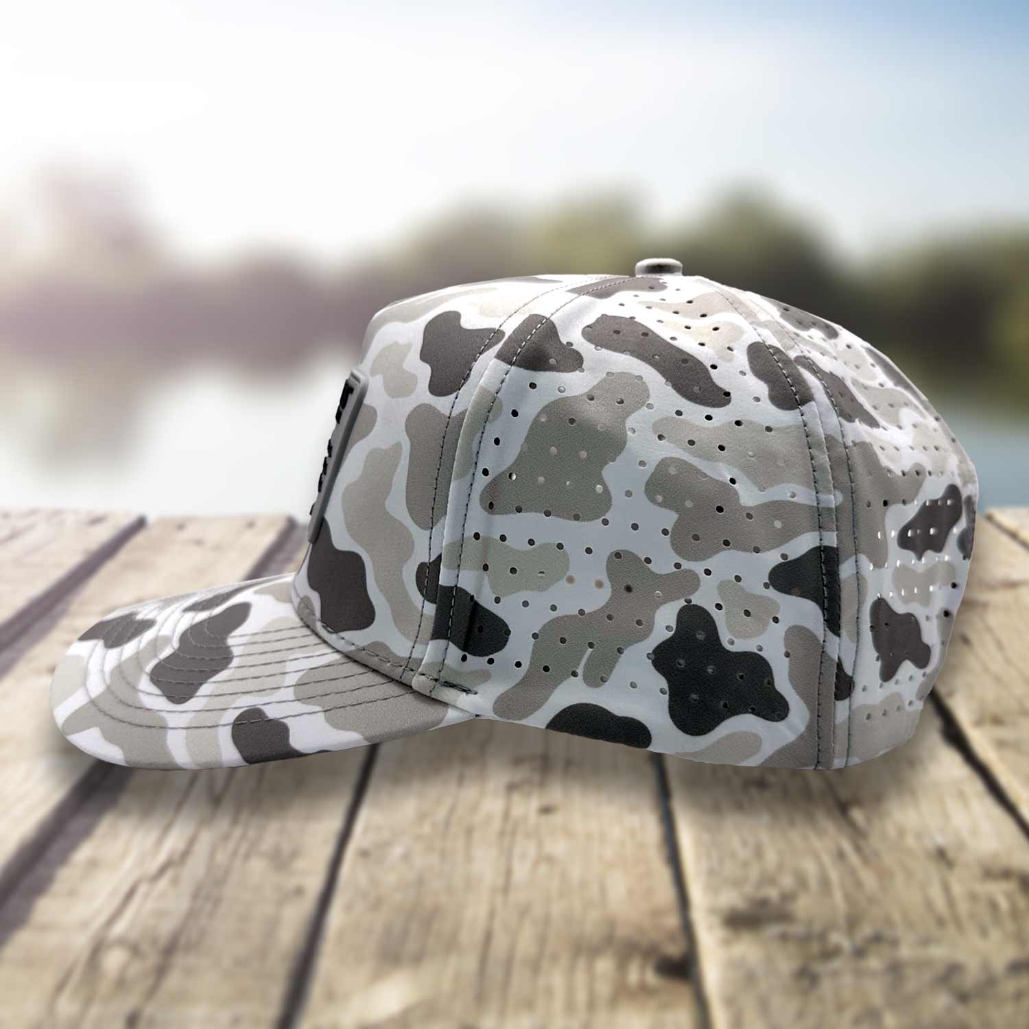 Side view of the Six Knots Coastal Camo Snapback Hat on a dock with a blurred marina backdrop, highlighting the breathable mesh back — water-resistant camo performance hat featuring a gray camouflage pattern; perfect for fishing, boating, and versatile coastal lifestyle wear.