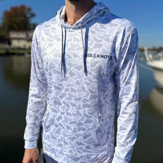 Man standing in a marina wearing the Six Knots Coastal Camo Performance Hoodie in the ‘Fogg’ colorway — lightweight, breathable, and moisture-wicking fishing hoodie with a gray camouflage pattern in light and dark tones; perfect for saltwater fishing, boating, and all-weather coastal adventures.