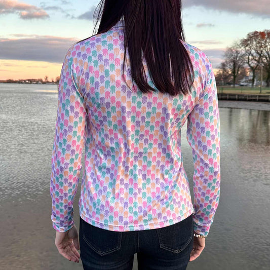 Rear view of woman on a dock at sunset wearing the Six Knots Don't Be Jelly Women's Performance Quarter Zip. This breathable, lightweight women's pullover features moisture-wicking fabric and a vibrant all-over jellyfish print in bold coastal colors — ideal for boating, fishing, beach outings, and active seaside adventures.