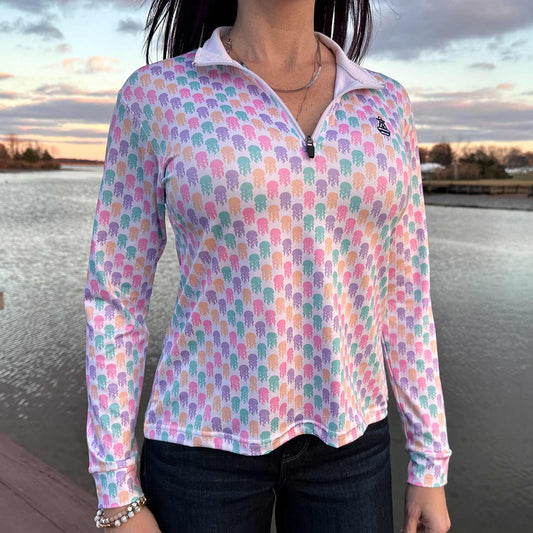 Woman standing on a dock by the water at sunset wearing the Six Knots Don't Be Jelly Women's Performance Quarter Zip. This lightweight, moisture-wicking quarter zip pullover features a vibrant all-over jellyfish print in bold coastal colors — perfect for boating, fishing, beach days, and active seaside adventures.