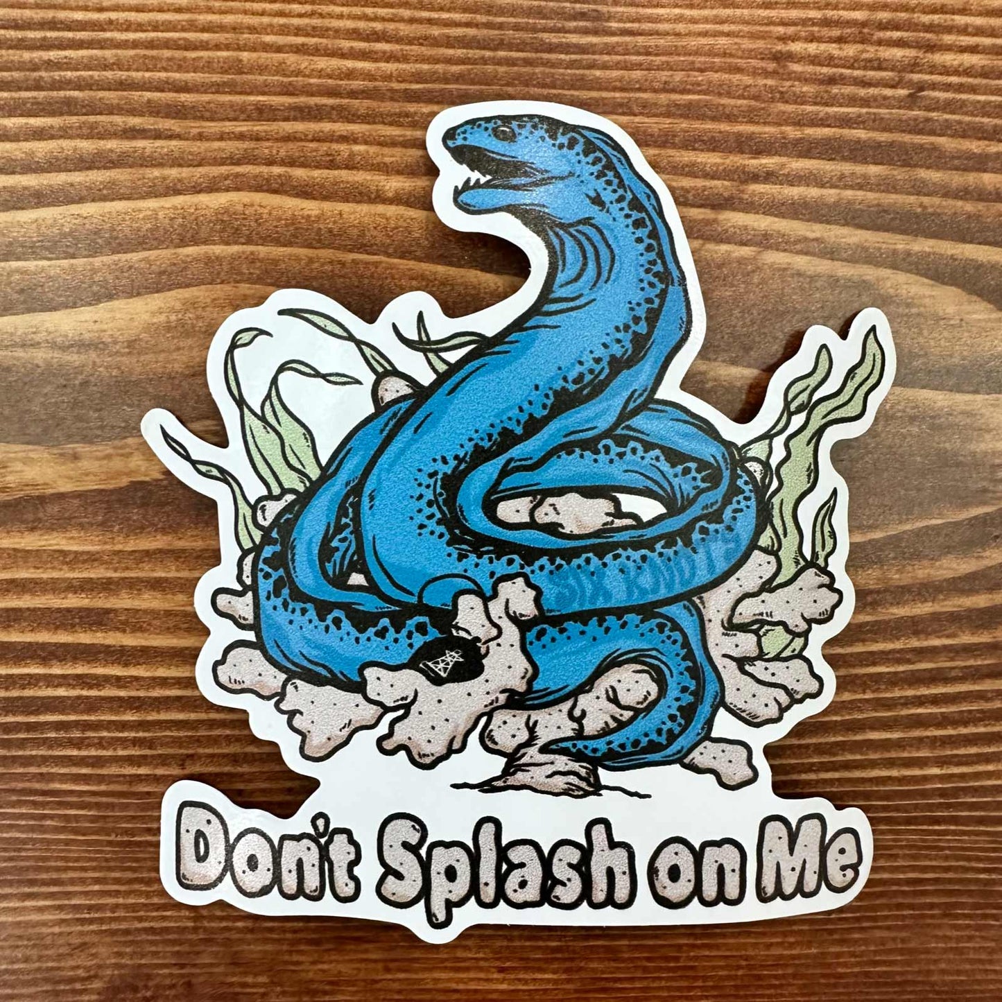 Overhead view of Six Knots "Don't Splash On Me" vinyl sticker featuring a bold blue eel entwined in seaweed, with hidden Six Knots buoy logo — durable, waterproof decal for coolers, boats, and outdoor gear