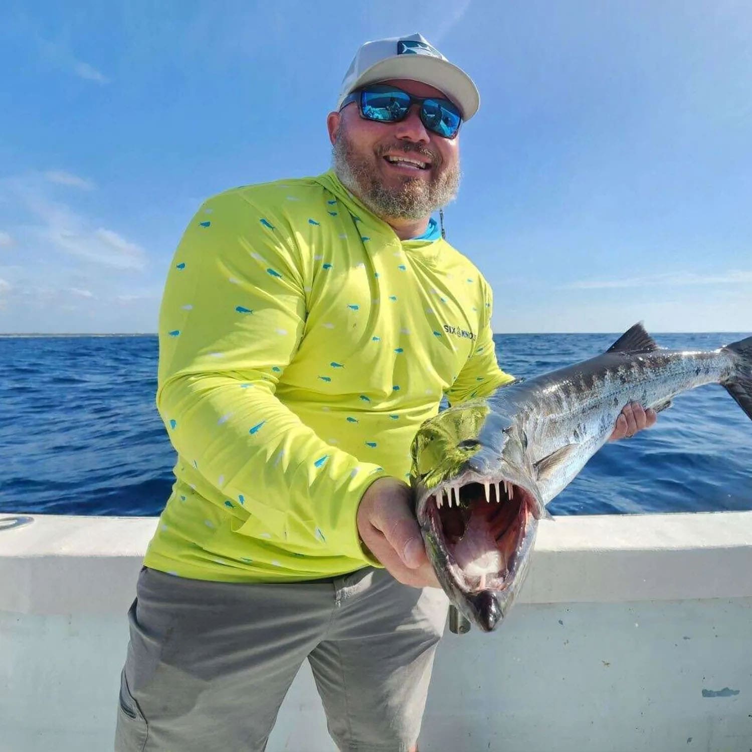Man holding a freshly caught fish on the deck of his boat, wearing the Six Knots Dorado Performance Hoodie — moisture-wicking, lightweight fishing apparel