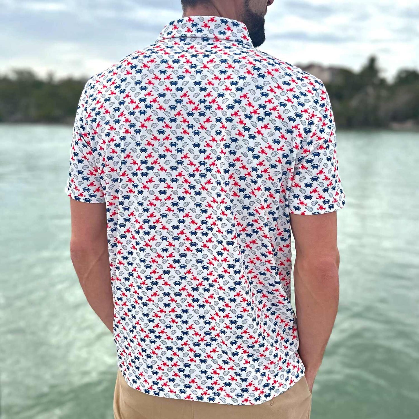 Rear view of a man on a Florida boat dock wearing the Six Knots East Coaster Performance Polo Shirt. This breathable, lightweight men's polo features a red, white, and blue all-over seafood print with iconic East Coast favorites like lobsters, crabs, and oysters. Designed for moisture-wicking comfort, it's ideal for boating, fishing, golf, beach outings, and coastal lifestyle wear