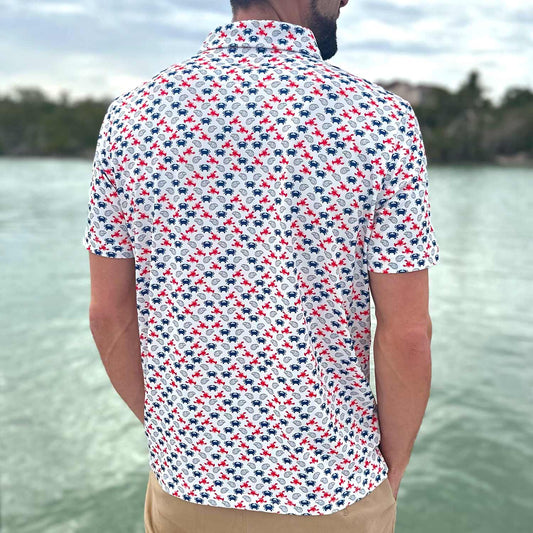 Rear view of a man on a Florida boat dock wearing the Six Knots East Coaster Performance Polo Shirt. This breathable, lightweight men's polo features a red, white, and blue all-over seafood print with iconic East Coast favorites like lobsters, crabs, and oysters. Designed for moisture-wicking comfort, it's ideal for boating, fishing, golf, beach outings, and coastal lifestyle wear
