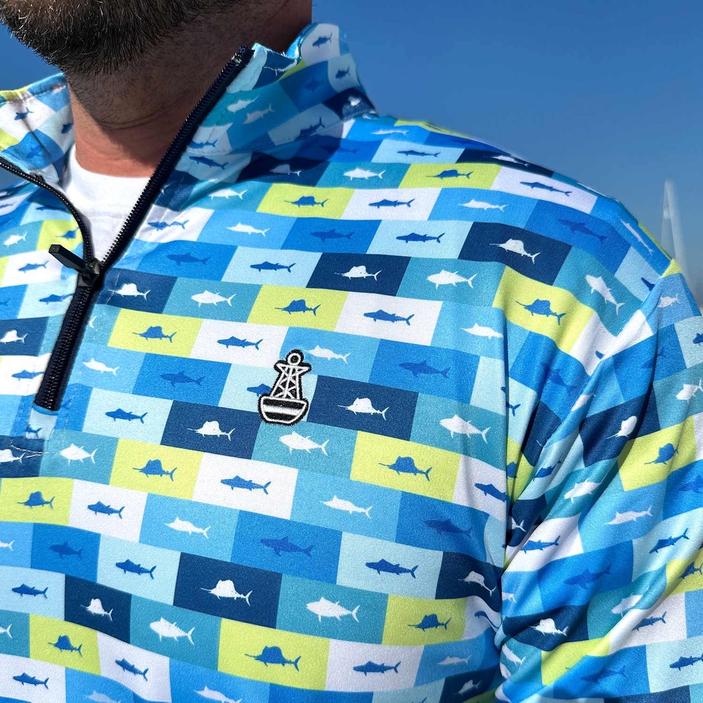Close-up detail of the Six Knots Fish Flag Men’s Performance Quarter Zip featuring the iconic Six Knots buoy logo — lightweight, breathable, and quick-dry men’s fishing pullover with a vibrant all-over print of sportfish framed in lime green, navy, light blue, and white nautical flag-style boxes; built for saltwater fishing, offshore boating, and all-weather coastal performance.