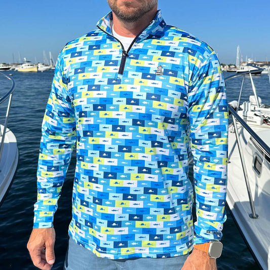 Man standing in a marina surrounded by powerboats wearing the Six Knots Fish Flag Men’s Performance Quarter Zip — lightweight, breathable, and moisture-wicking fishing pullover featuring an all-over fish pattern framed in lime green, navy blue, light blue, and white flag-style boxes; ideal for saltwater angling, offshore boating, and versatile all-weather coastal adventures.