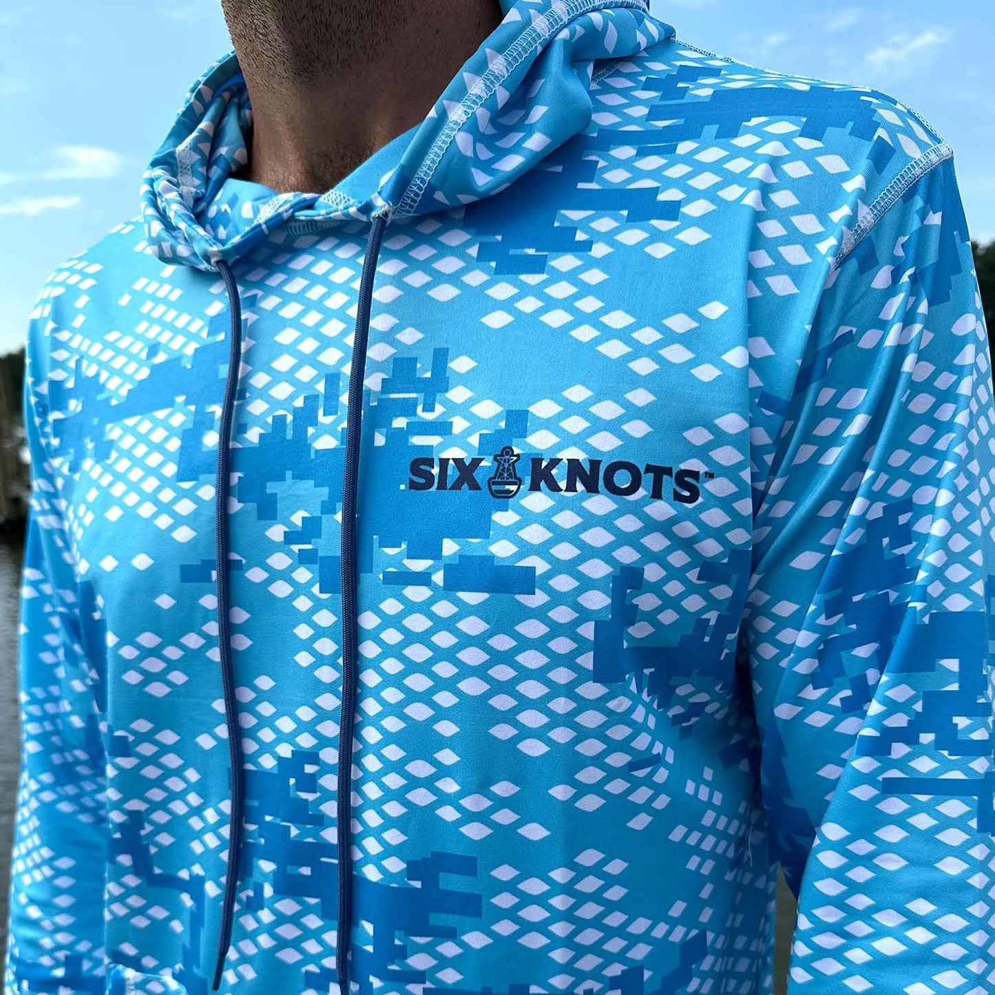 Close-up detail of the Six Knots Fish Scale Camo Performance Hoodie in blue, featuring a bold digital camouflage pattern inspired by fish scales and the classic Six Knots wordmark — a high-performance fishing hoodie that’s lightweight, breathable, moisture-wicking, and UPF sun-protective; built for saltwater fishing, offshore boating, and rugged coastal adventures in any weather.