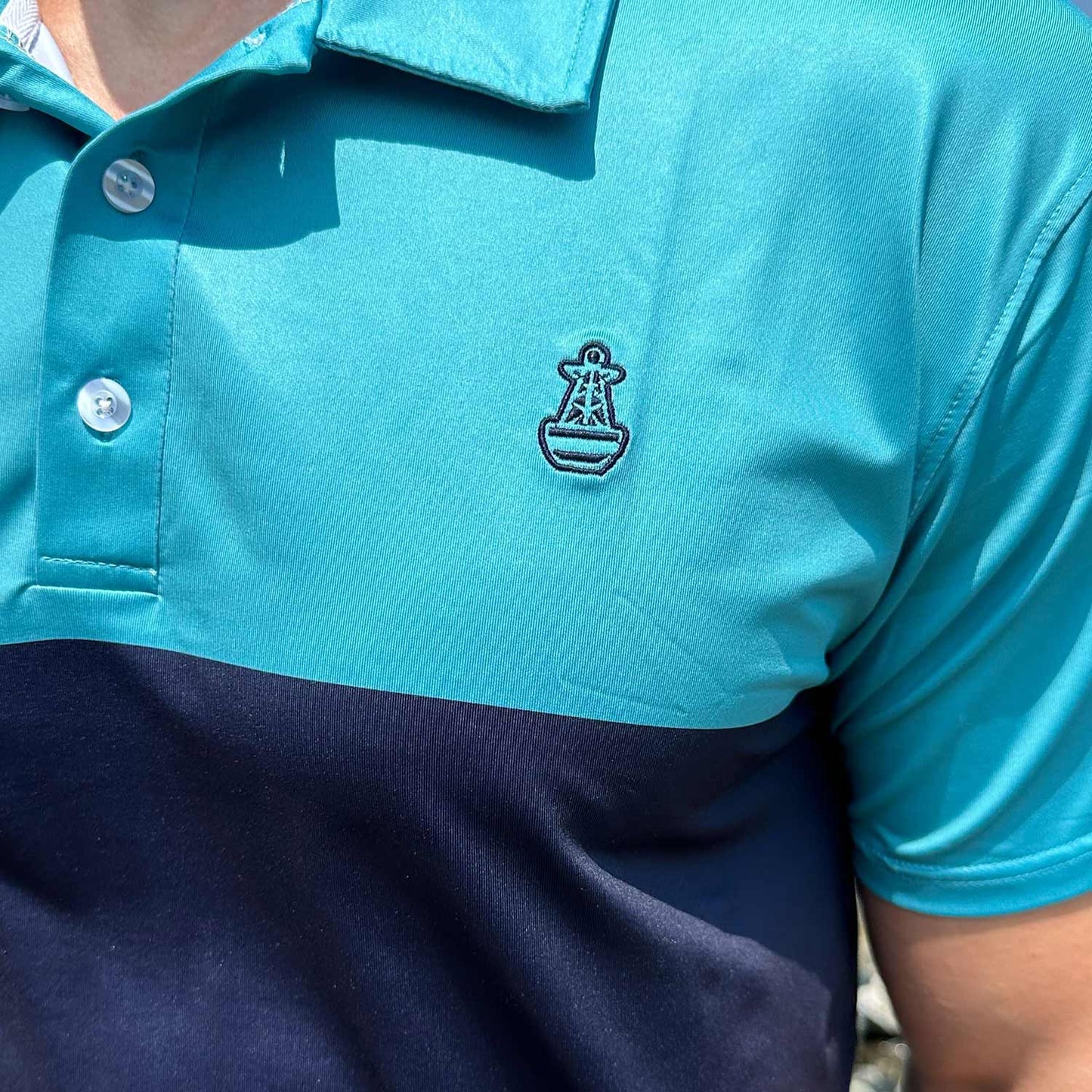 Close-up detail of the Six Knots Into The Blue Performance Polo Shirt showcasing two bold blue stripes—robin's egg blue and navy—crafted in lightweight, moisture-wicking fabric. Features the signature Six Knots buoy logo on the chest, ideal for coastal style, boating, golfing, and all-day comfort in warm weather.