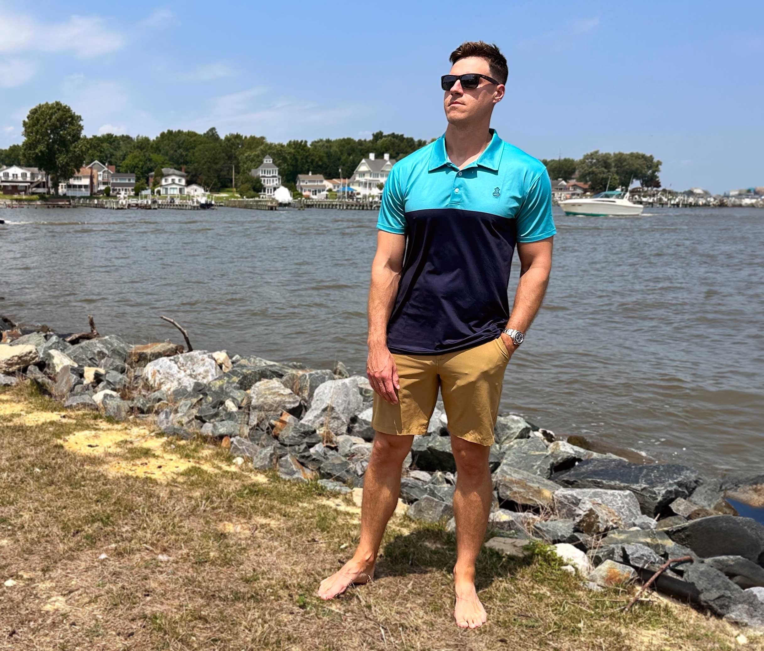 Man in blue polo shirt and sunglasses standing on the grass in front of a lake