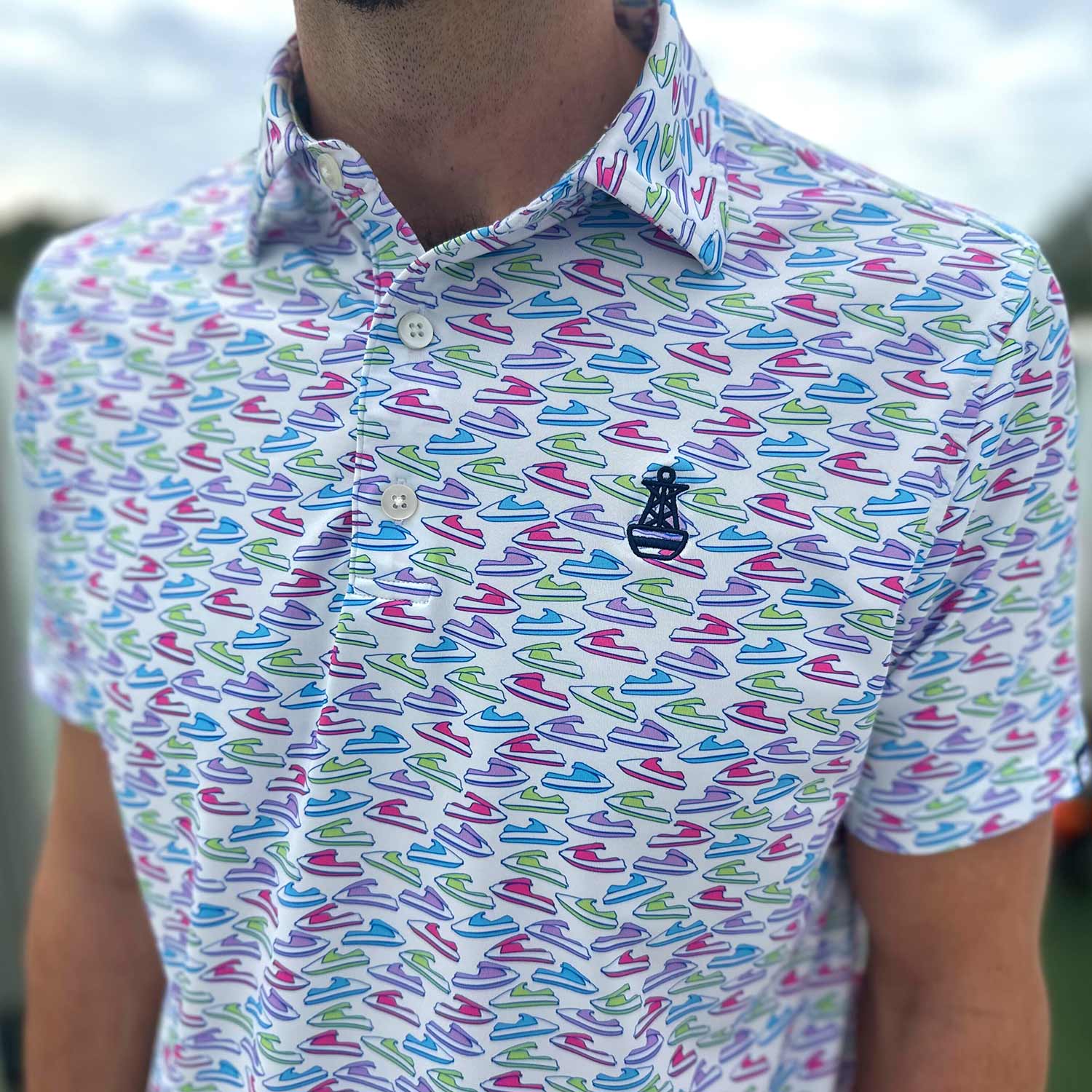 Close-up detail of the Six Knots Just Send It Performance Polo Shirt, showcasing its vibrant all-over jet ski print in blue, green, pink, and purple. This lightweight, breathable men's polo shirt features moisture-wicking fabric designed for comfort and performance. Ideal for boating, jet skiing, golfing, beach trips, and everyday coastal lifestyle wear.
