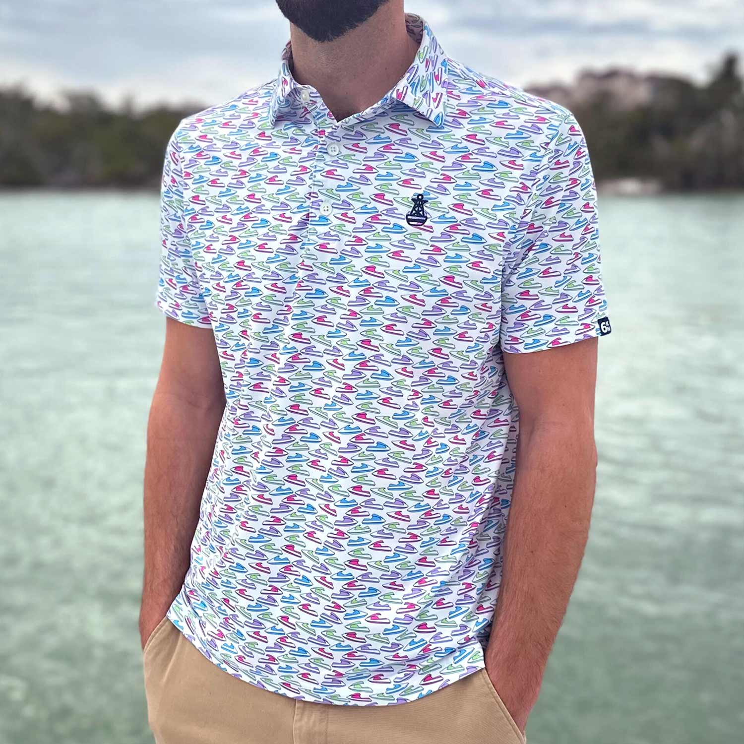 Man standing on a dock in Florida wearing the Six Knots Just Send It Performance Polo Shirt. This lightweight, breathable men's polo shirt features moisture-wicking fabric and a vibrant all-over jet ski print in blue, green, pink, and purple. Ideal for boating, jet skiing, golfing, beach outings, and everyday coastal lifestyle wear.