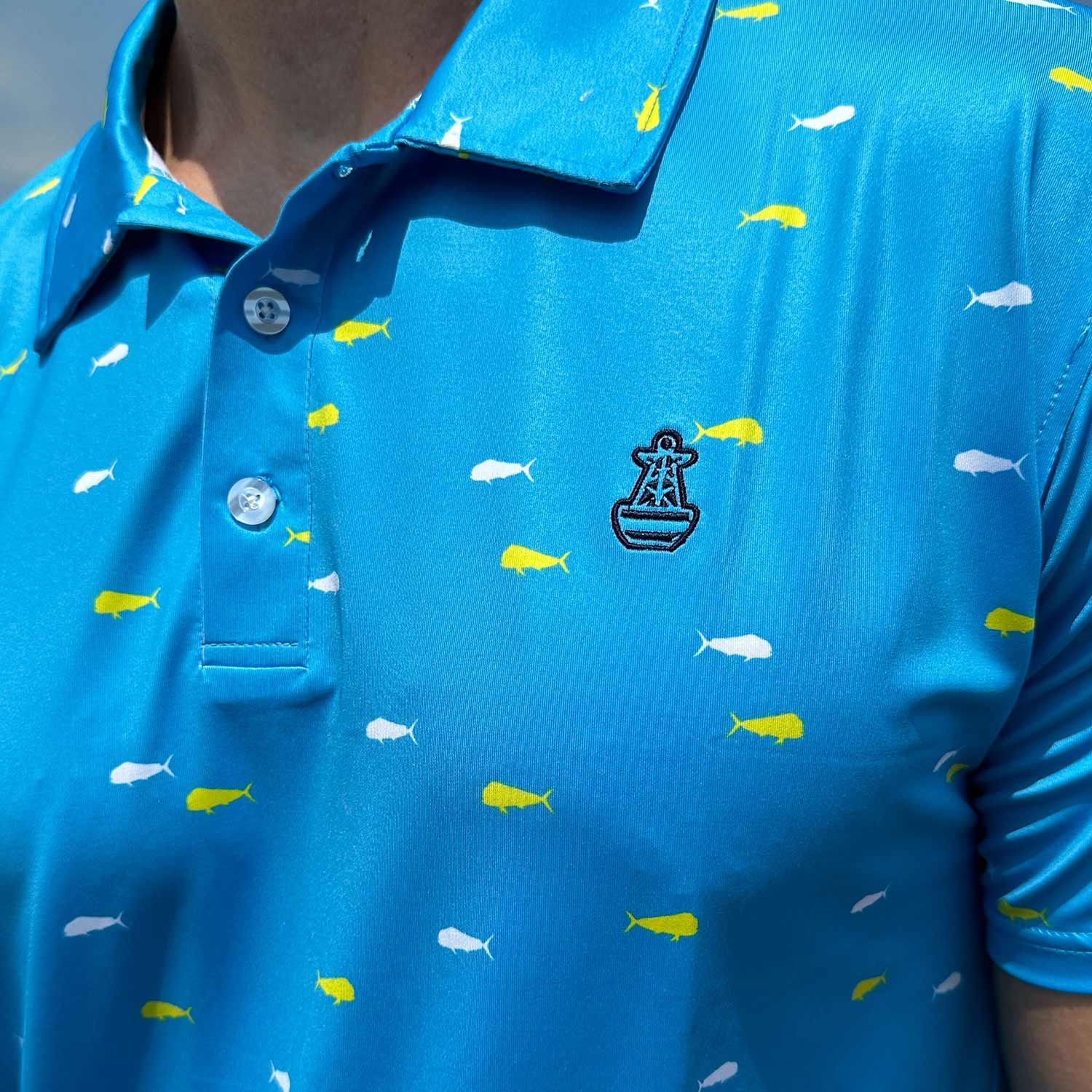 Close-up detail of the vibrant blue Six Knots Mahi Mahi Performance Polo Shirt showcasing the signature Six Knots buoy logo on the chest. This men's polo features a bold white and yellow mahi mahi fish print, lightweight moisture-wicking fabric, and built-in UPF 50+ sun protection. Designed for performance and comfort, it's perfect for boating, golf, beach outings, and active coastal lifestyles.