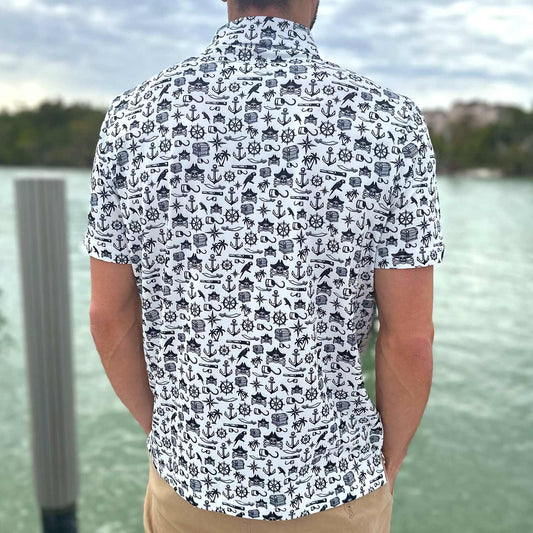 Rear view of a man standing on a dock in Florida wearing the Six Knots Pirate's Life Performance Polo Shirt. This breathable, lightweight men's polo features moisture-wicking fabric and a bold black and white nautical pirate print with treasure chests, skull and crossbones, cannons, hooks, and maritime symbols. Ideal for boating, golfing, beach outings, and coastal adventures.