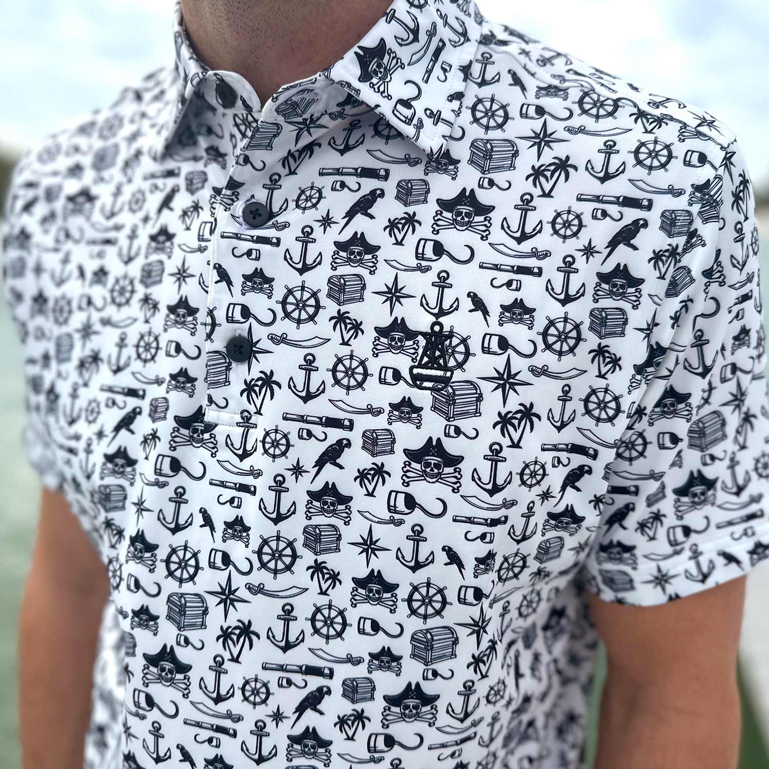 Close-up of the Six Knots Pirate's Life Performance Polo Shirt, highlighting its detailed black and white nautical pirate print. This lightweight, breathable men's polo shirt is made with moisture-wicking fabric and features intricate designs including treasure chests, skull and crossbones, cannons, hooks, and maritime symbols. Perfect for boating, golf, beach trips, and coastal lifestyle wear.