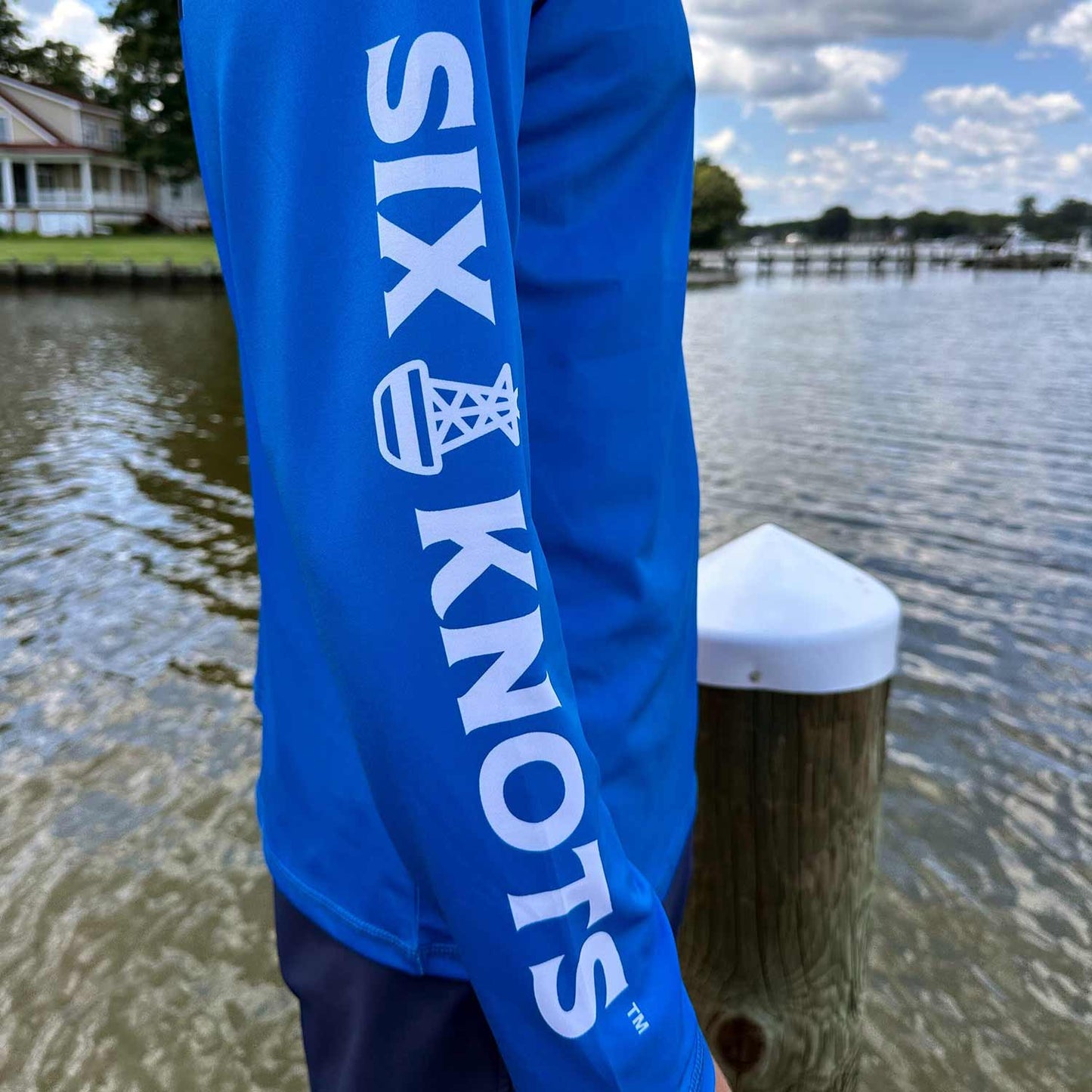 Close-up sleeve detail of the Six Knots Red Sky At Night Men’s Performance Crew in royal blue, showcasing the bold full-length Six Knots wordmark — lightweight, breathable, and moisture-wicking men’s fishing shirt in a vibrant royal blue color; built with UPF sun protection and quick-dry fabric for saltwater fishing, offshore boating, and high-performance coastal adventures in any weather.