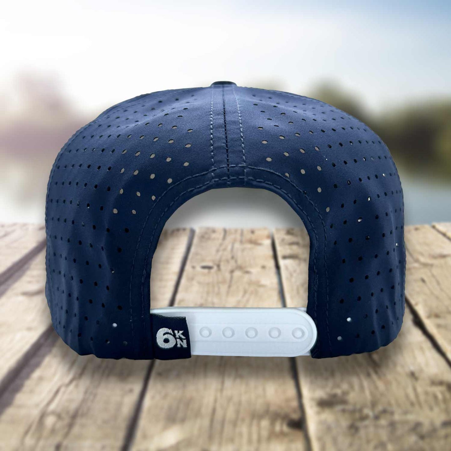 Back view of the Six Knots Red Sky At Night Snapback Hat on a dock with a blurred marina backdrop, showcasing the breathable white mesh back and adjustable snapback closure — durable, water-resistant performance fishing hat in a crisp white and navy blue colorway; ideal for saltwater fishing, offshore boating, and all-weather coastal lifestyle adventures.