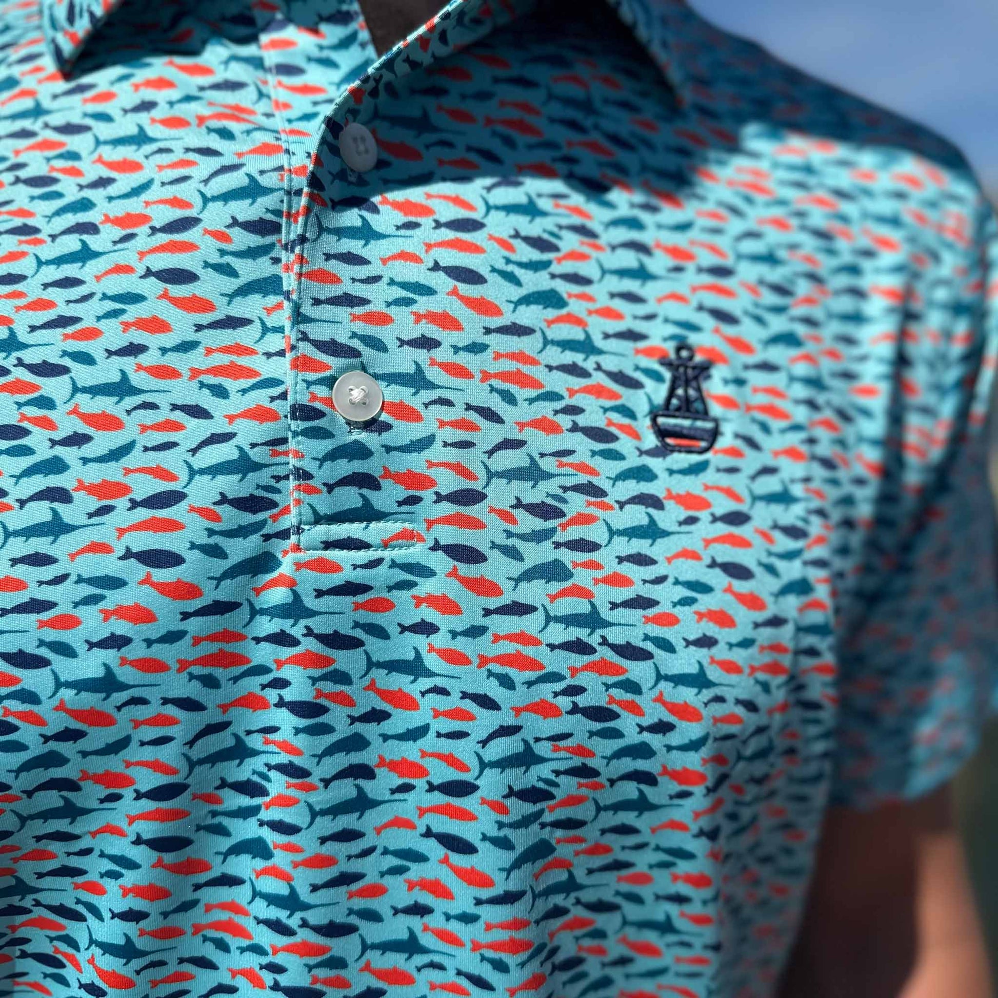 Close-up of Six Knots Schoolie Performance Polo Shirt featuring vibrant fish pattern, button detail, and Buoy logo — lightweight, moisture-wicking polo ideal for fishing, boating, and golfing