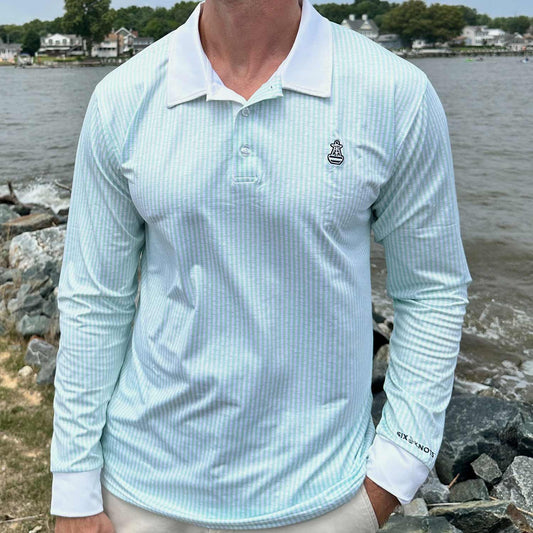 Man standing by coastal rocks and water wearing the Six Knots Seafarer Performance Polo Shirt with mint green seersucker stripes. This lightweight, long-sleeve men's polo is made with moisture-wicking, breathable fabric for superior comfort, UV sun protection, and all-weather performance. Perfect for saltwater fishing, boating, seaside travel, and active coastal lifestyles.