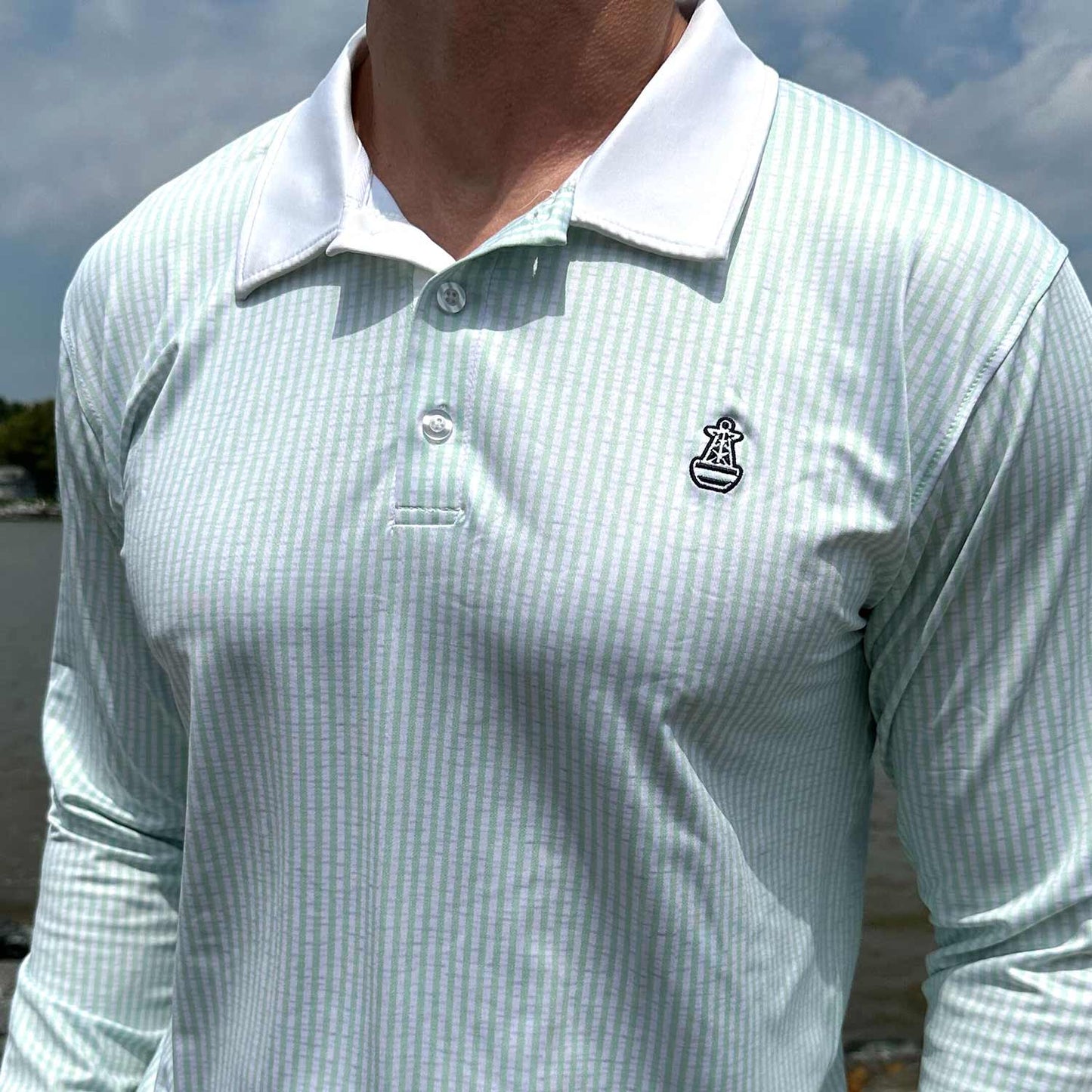 Close-up detail of the Six Knots Seafarer Performance Polo Shirt featuring mint green seersucker stripes and a Six Knots buoy logo on the chest. This lightweight, long-sleeve men's  polo is crafted from breathable, moisture-wicking fabric with built-in UPF sun protection. Perfect for all-day comfort and high-performance during offshore fishing, boating, coastal travel, and active seaside adventures.