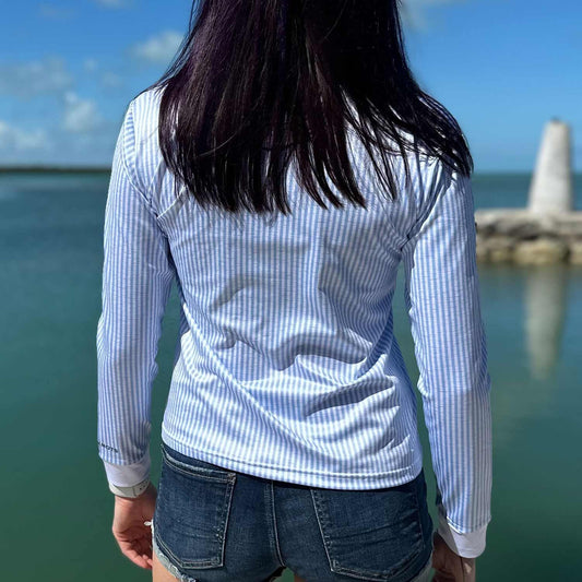 Rear view of a woman standing on a marina dock wearing the Six Knots Seafarer Women's Performance Quarter Zip with blue seersucker stripes — all-weather, moisture-wicking pullover offering UPF sun protection and breathable comfort for fishing, sailing, boating, and coastal adventures