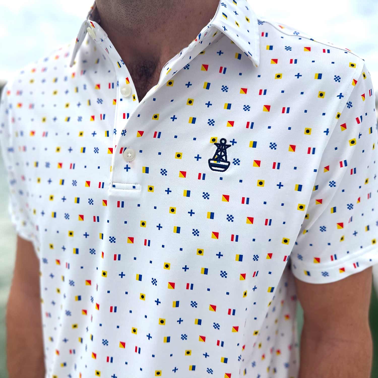 Close-up detail of the Six Knots Signal Flag Performance Polo Shirt. This lightweight, breathable men's performance polo features moisture-wicking fabric and a vibrant all-over nautical signal flag pattern that spells out 'Six Knots.' Designed for sailing, boating, beach outings, and everyday coastal lifestyle wear