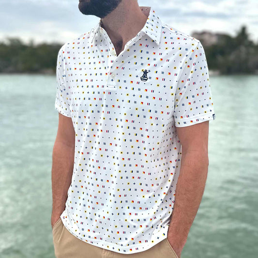Man standing on a boat dock in Florida wearing the Six Knots Signal Flag Performance Polo Shirt. This lightweight, moisture-wicking men's polo features a repeating nautical signal flag pattern that spells out 'Six Knots' — perfect for sailing, boating, golfing, coastal living, and summer style