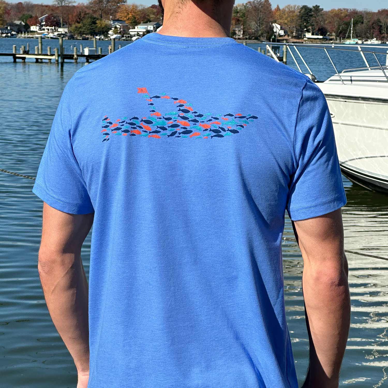 Rear view of man at a Maryland marina wearing the blue Six Knots Sink or Swim Classic T-Shirt. This ultra-soft, lightweight unisex tee is made from a breathable cotton-polyester blend and features a detailed back graphic of a boat formed by a school of fish. Ideal for everyday wear, weekend lounging, beach trips, coastal vacations, casual outings, and relaxed waterfront living.