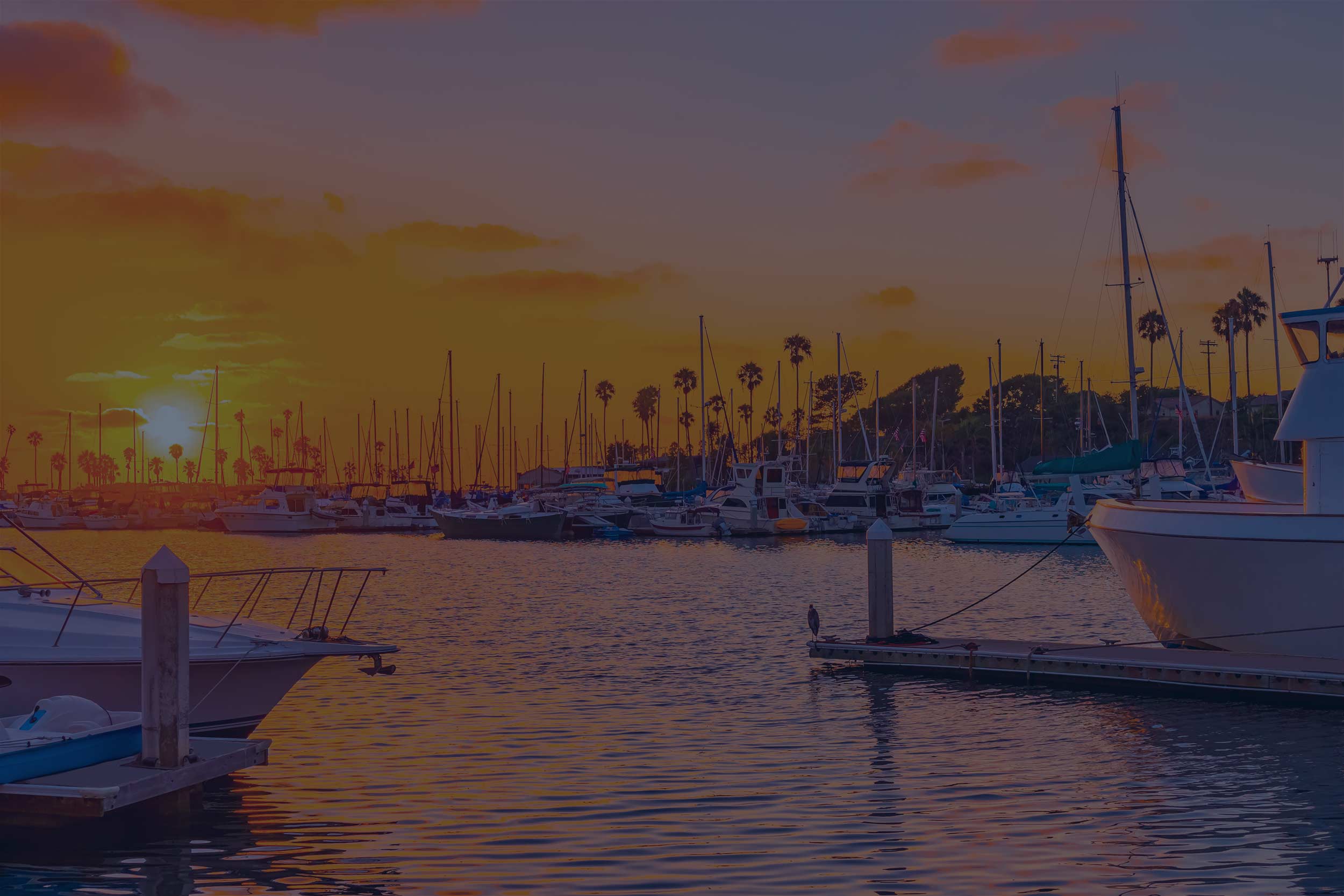 Scenic sunset over marina with boats docked, highlighting coastal lifestyle and evening waterfront views.