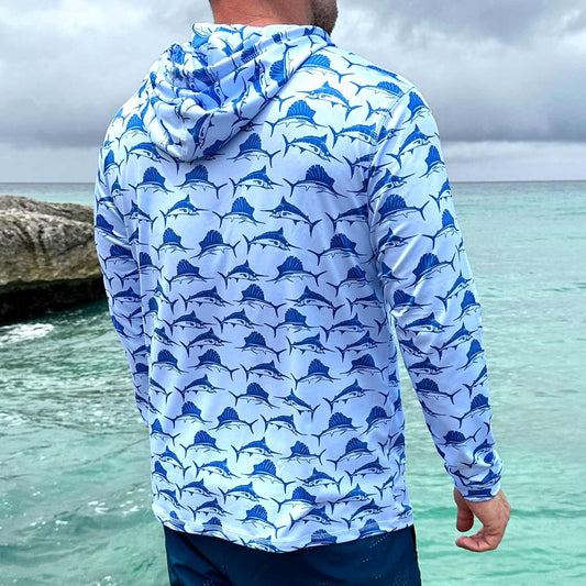 Rear view of man near the water in St. Maarten wearing the Six Knots Swords and Sails Performance Hoodie — lightweight, moisture-wicking fishing apparel featuring a nautical pattern with swordfish and marlins