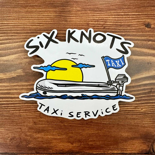 Overhead view of Six Knots "Taxi Service" vinyl sticker featuring an inflatable lifeboat silhouette against a bold yellow sunrise — durable, waterproof decal ideal for coolers, tumblers, tackle boxes, water bottles, and marine gear