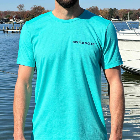 Man at a Maryland marina wearing the seafoam green Six Knots Maryland Crab Classic T-Shirt. This lightweight, ultra-soft unisex tee is made from a breathable cotton-polyester blend and features a subtle Six Knots wordmark on the chest. Perfect for everyday wear, weekend relaxation, coastal getaways, casual outings, and easygoing waterfront style.