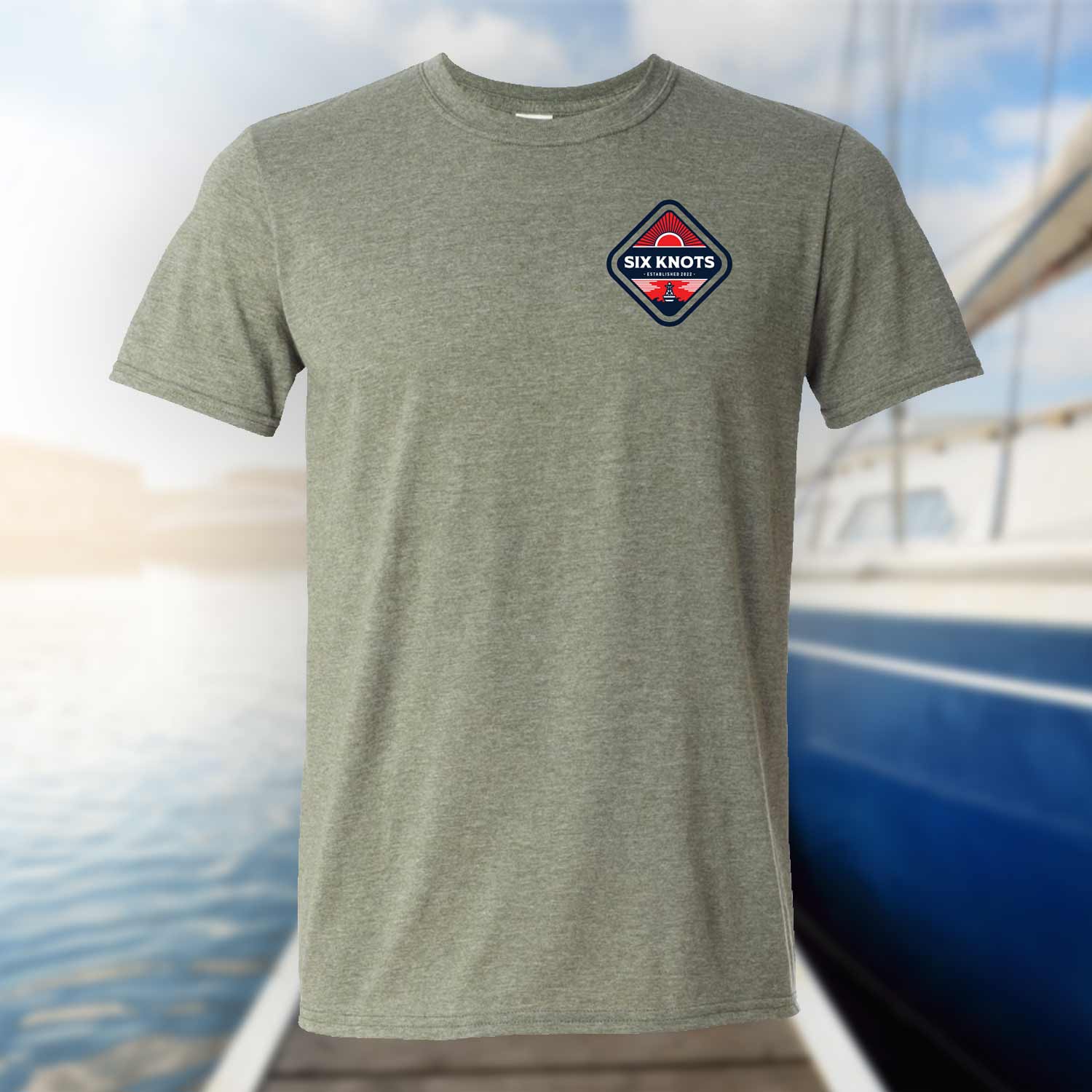 Six Knots Red Sky At Night Classic T-Shirt in heather gray displayed against a blurred marina backdrop, featuring a subtle chest badge with the Six Knots wordmark and bold red rising sun graphic. This ultra-soft, lightweight unisex cotton-polyester blend tee delivers breathable, all-day comfort—ideal for saltwater fishing, coastal adventures, beach mornings, and laid-back seaside layering.