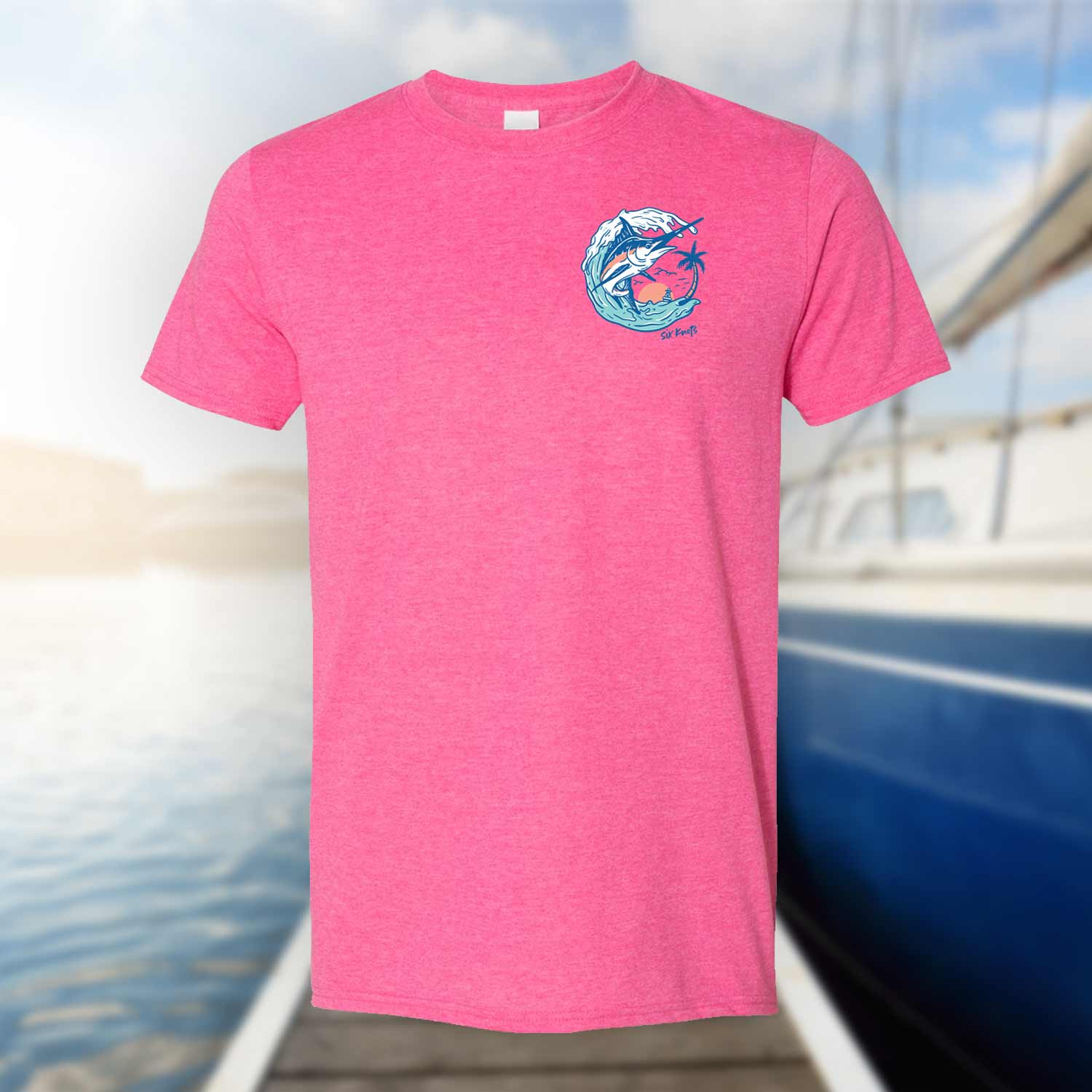 Six Knots Summer Catch Classic T-Shirt in vibrant pink displayed against a blurred marina background, featuring a front chest badge with a marlin jumping from the water. This lightweight, ultra-soft unisex cotton-polyester blend t-shirt offers breathable, all-day comfort—ideal for saltwater fishing, beach mornings, coastal getaways, and relaxed oceanfront adventures.