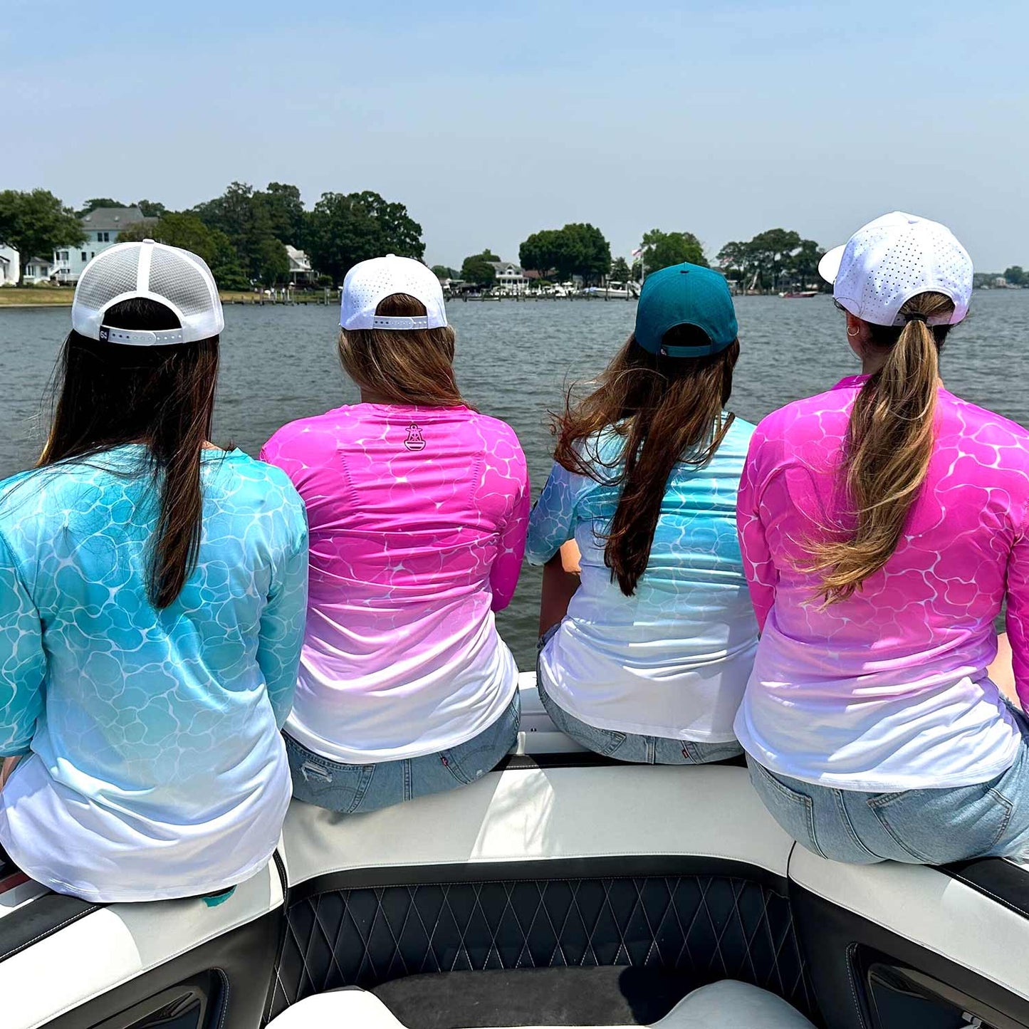 Rear view of women relaxing on a powerboat wearing the Six Knots Surf Fisher Women's Performance Crew, styled with Six Knots Snapback Hats. These long-sleeve women's fishing shirts showcase a bold, water-inspired print, crafted from ultra-lightweight, moisture-wicking fabric with built-in UPF 50+ sun protection. Engineered for saltwater fishing, offshore boating, beach outings, and active coastal lifestyles, they offer breathable comfort and elevated performance apparel for life on the water.