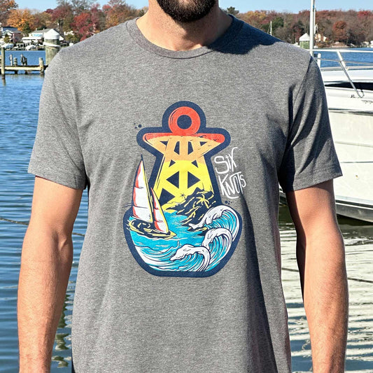 Man at a Maryland marina wearing the dark gray Six Knots Tropical Storm Classic T-Shirt. This ultra-soft, lightweight unisex tee is crafted from a breathable cotton-polyester blend and features a large Six Knots buoy logo with a detailed sailboat-in-a-storm graphic, swirling waves, and bold Six Knots lettering. Ideal for everyday wear, weekend lounging, beach vacations, casual coastal outings, and relaxed waterfront style.