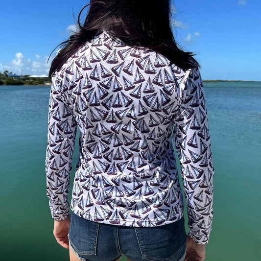 Rear view of a woman standing on a marina dock wearing the Six Knots Under Sail Women's Performance Quarter Zip featuring a repeating hand-sketched sailboat pattern — lightweight, breathable, and moisture-wicking pullover with UPF sun protection and all-weather comfort, ideal for fishing, boating, sailing, and coastal lifestyle activities