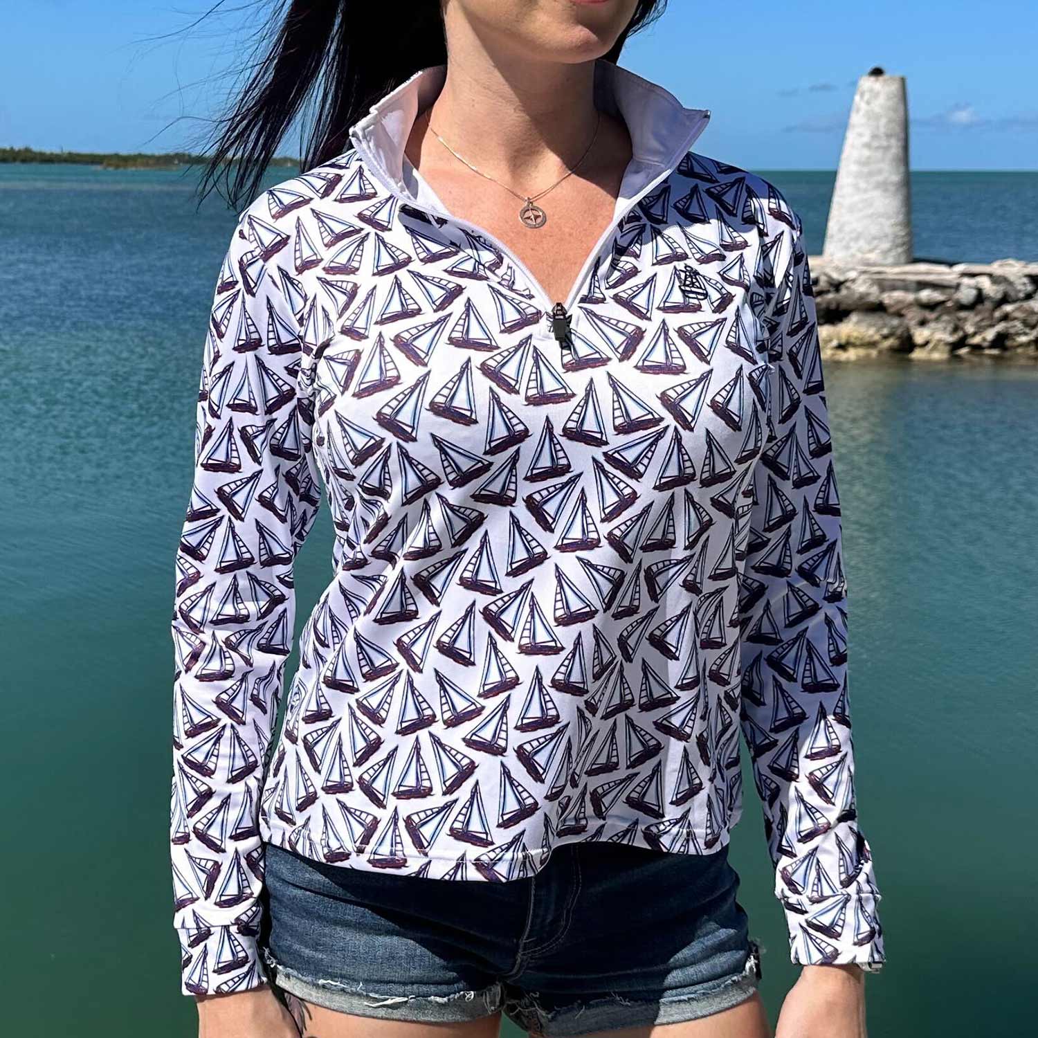 Woman standing on a marina dock wearing the Six Knots Under Sail Women's Performance Quarter Zip featuring a repeating hand-sketched sailboat pattern — lightweight, moisture-wicking, and breathable pullover with UPF sun protection and all-weather comfort, perfect for fishing, boating, sailing, and coastal lifestyle adventures