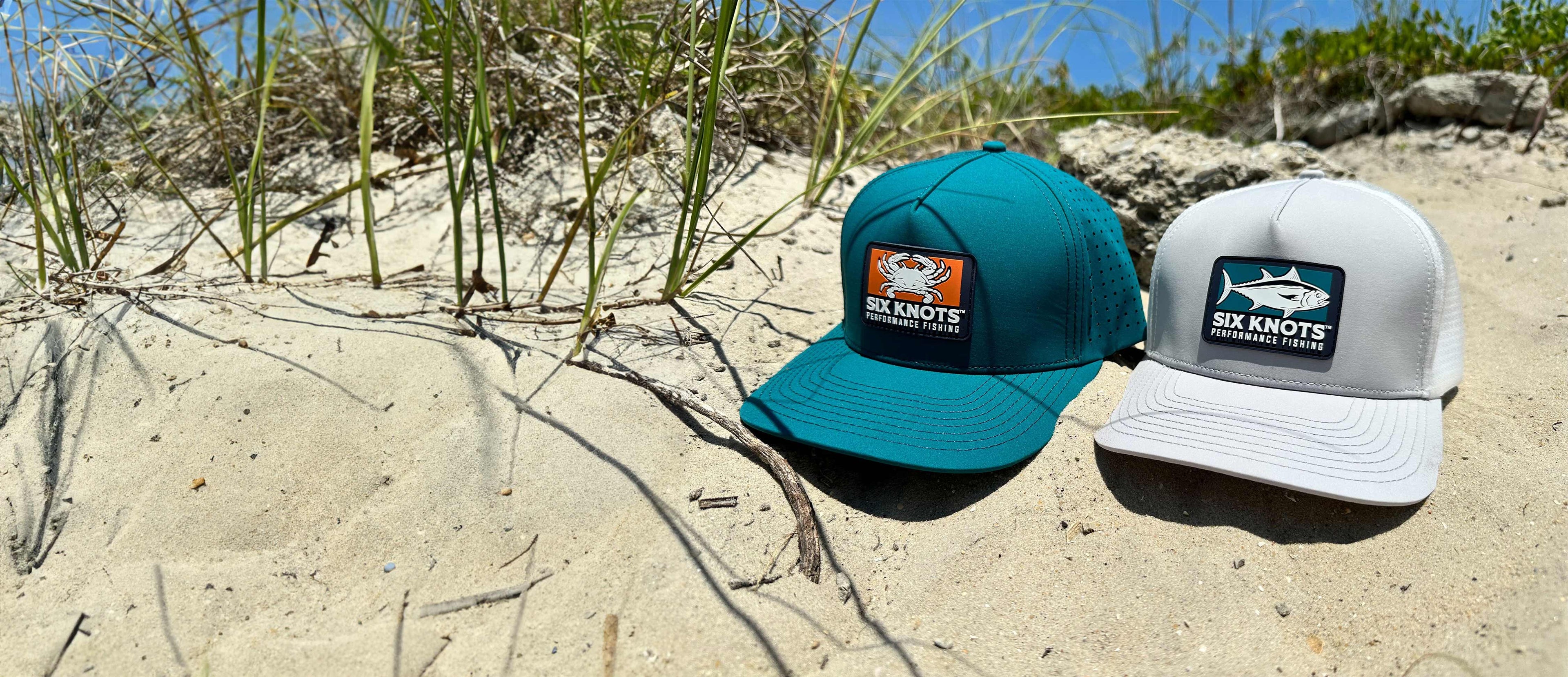 Six Knots water resistant hats sitting in the sand on a beach in North Carolina