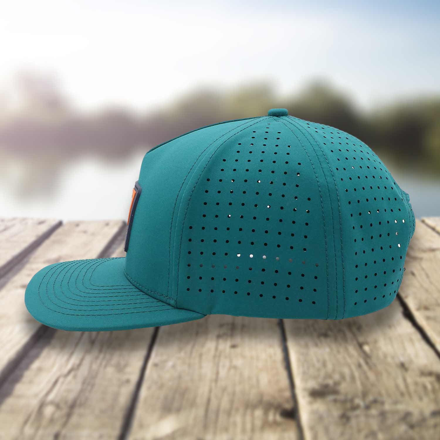 Side profile view of Six Knots Waterman Snapback Hat resting on a dock with a blurred marina backdrop. This eye-catching teal, water-resistant snapback features a bold front patch with a Maryland blue crab and 'Six Knots Performance Fishing' logo. Engineered for coastal durability, breathability, and sun protection, it's the ultimate hat for saltwater fishing, offshore boating, beach outings, and all-weather coastal adventures.