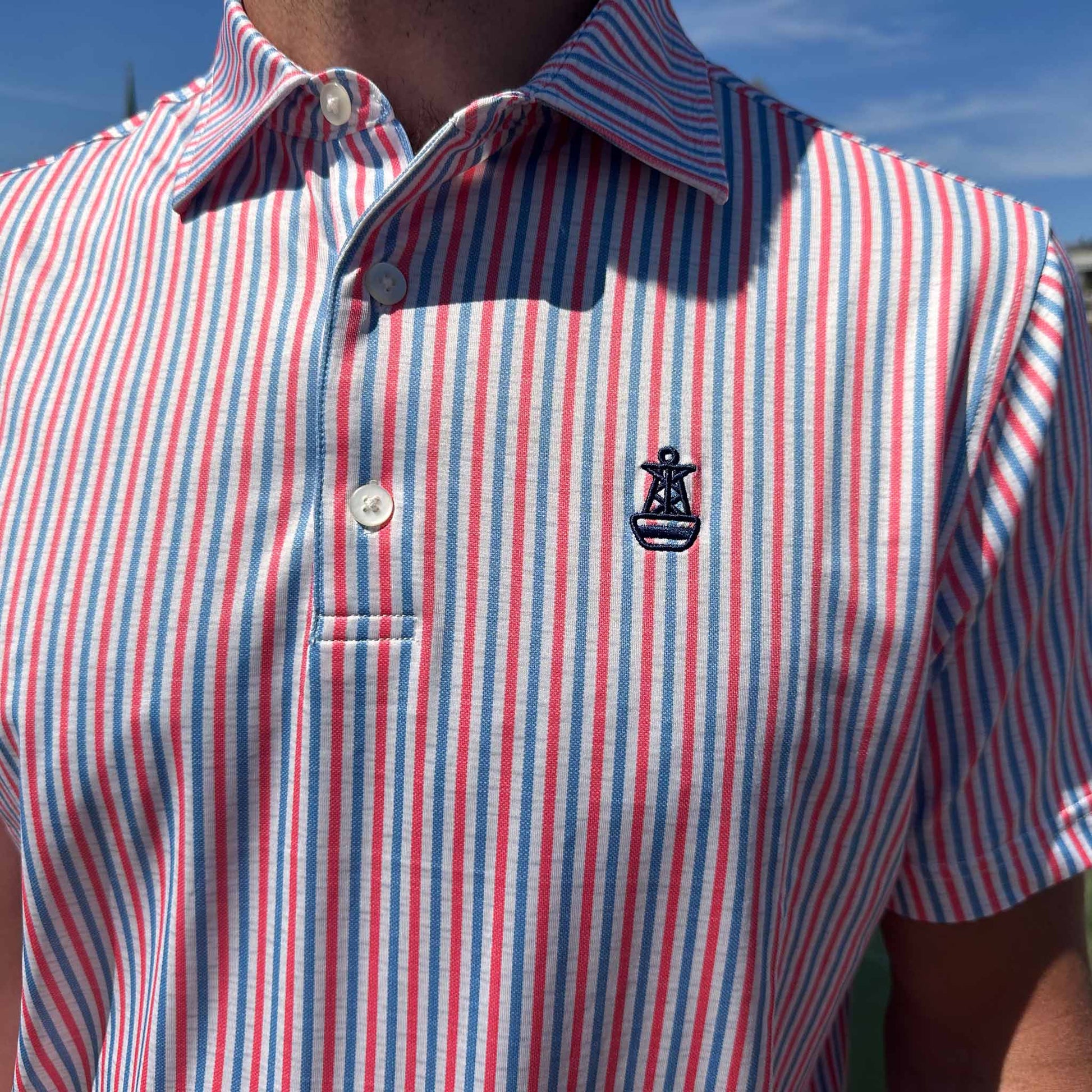 Close-up of the front of the Six Knots All American Performance Polo Shirt featuring the signature buoy logo and patriotic red, white, and blue seersucker stripes — lightweight, moisture-wicking men's polo ideal for fishing, boating, golf, and summer wear