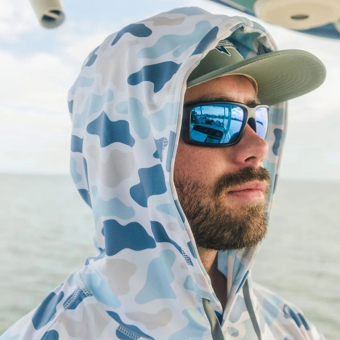 Man in sunglasses on a boat Fort Lauderdale, Florida wearing Six Knots Coastal Camo Performance Hoodie – Marsh Pattern with Hood Up, a lightweight moisture-wicking men's fishing hoodie