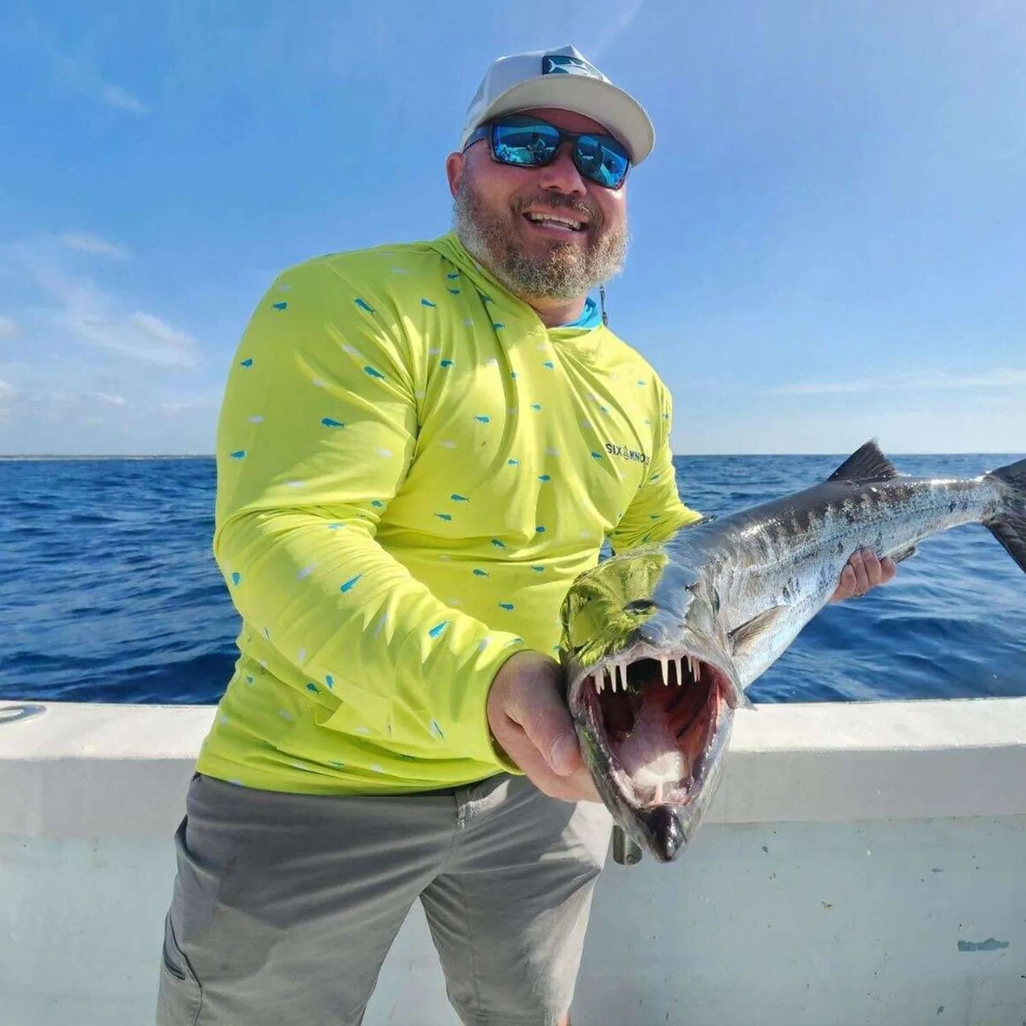 Man holding a freshly caught fish on the deck of his boat, wearing the Six Knots Dorado Performance Hoodie — moisture-wicking, lightweight fishing apparel